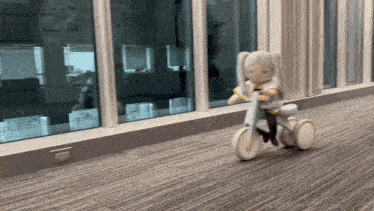 a doll is riding a tricycle on a hallway