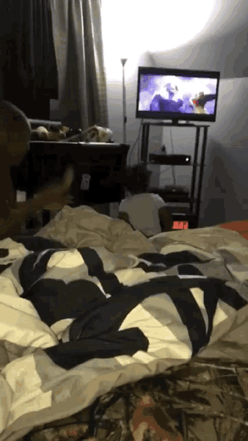 a person laying on a bed watching a television