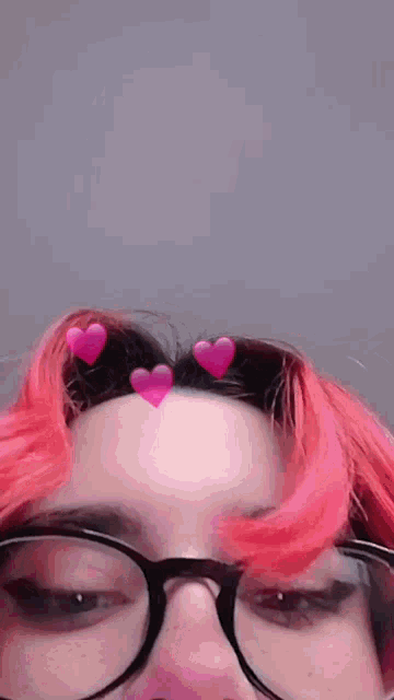a girl with pink hair and glasses has two pink hearts on her hair .