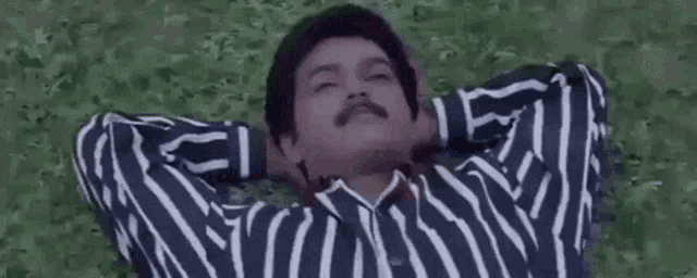 a man with a mustache is laying on the grass with his arms behind his head .