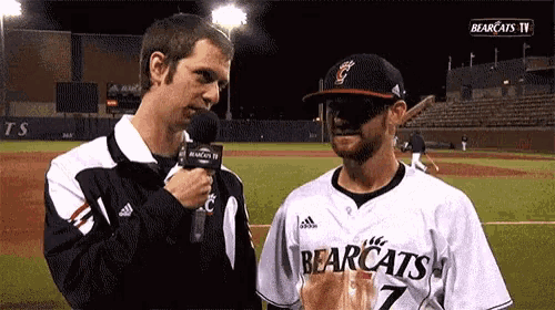 a man in a bearcats jersey talks to another man