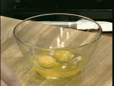 a glass bowl filled with eggs sits on a wooden surface