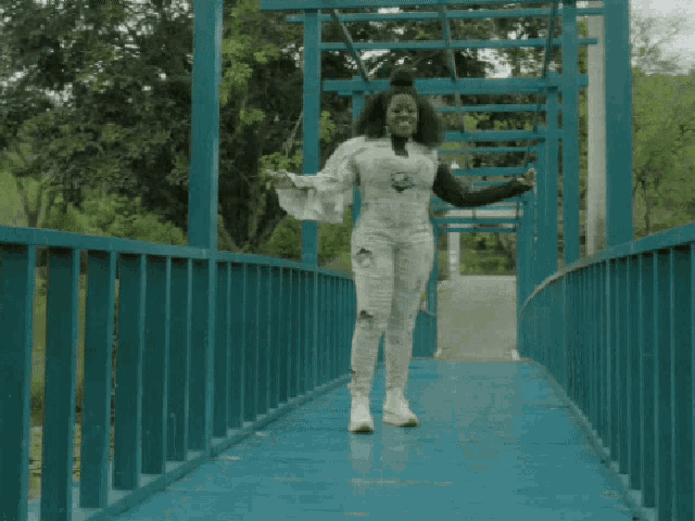 a woman in a white jumpsuit is walking across a bridge