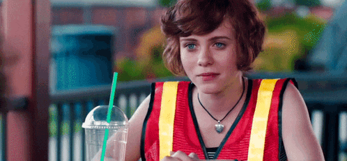 a woman wearing a red vest and a yellow vest is drinking from a plastic cup with a green straw
