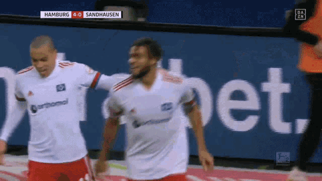 two soccer players are celebrating a goal in front of a banner that says " bet "