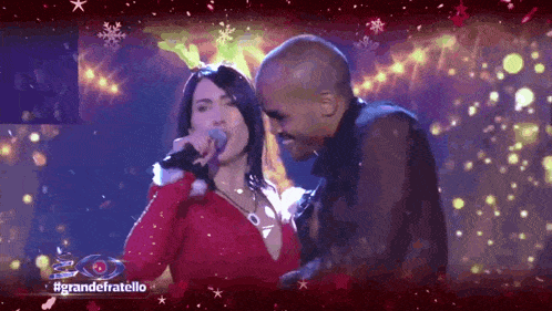 a woman singing into a microphone next to a man on a stage with #grandefratello written on the bottom