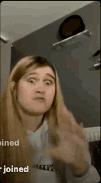 a girl with long blonde hair is making a funny face while giving the middle finger .