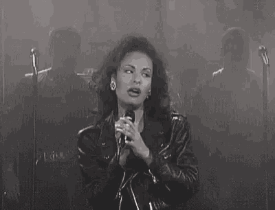 a black and white photo of a woman singing into a microphone on stage .