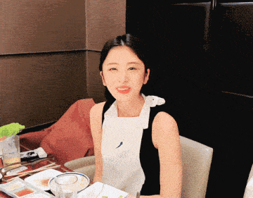 a woman in an apron sits at a table with plates and a glass