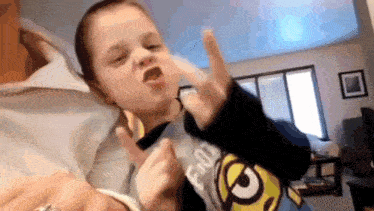 a little boy wearing a minion shirt is making a funny face while being held by a woman .