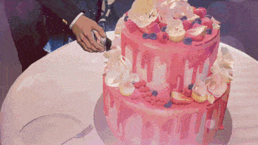 a man is cutting a pink cake with flowers and berries
