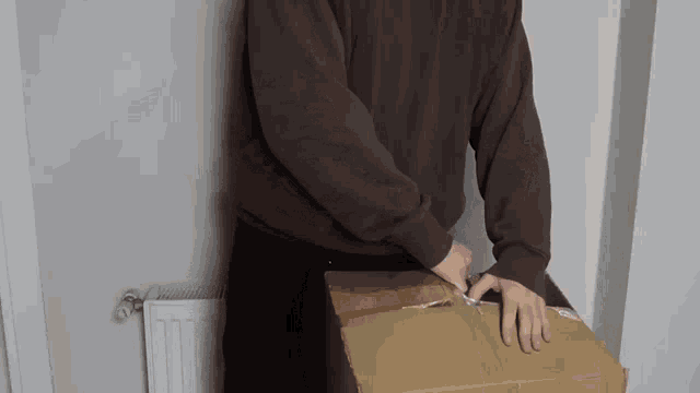 a man in a brown sweater is holding a cardboard box with a sticker on it that says ' fragile '