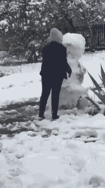 a person is standing in the snow near a large snowman