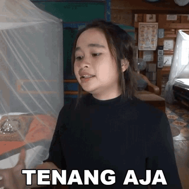 a woman in a black shirt is standing in front of a mosquito net and says tenang aja .