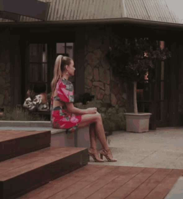 a woman in a pink dress sits on the steps of a building