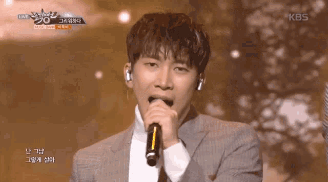 a man in a suit singing into a microphone with a kbs logo in the background