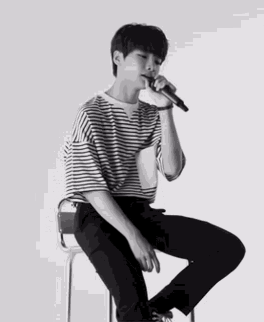 a young man in a striped shirt sits on a stool