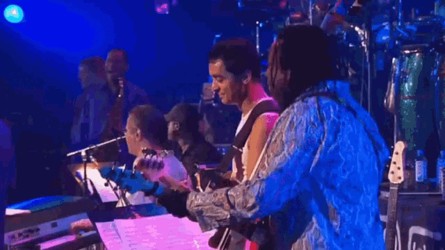 a man in a blue shirt is playing a guitar while another man looks on
