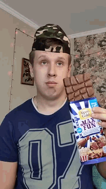 a man wearing a camouflage hat is holding a bar of alpen gold max fun