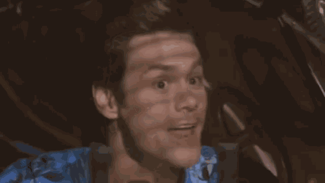a man in a blue shirt is sitting in a car and making a face .