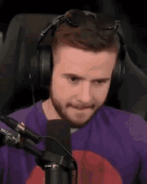 a man wearing headphones and sunglasses is sitting in front of a microphone and making a funny face .