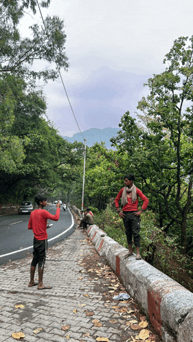 a man in a red shirt stands on the side of a road pointing at something