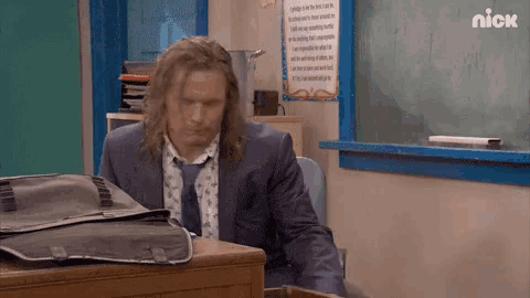 a man in a suit and tie is sitting at a desk in front of a chalkboard with the nick logo