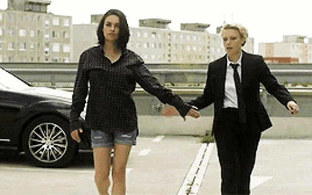two women are walking in a parking lot holding hands .