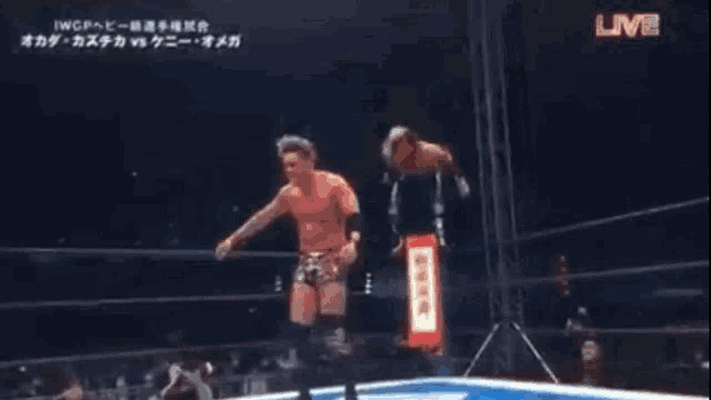 two men are wrestling in a ring with a sign that says live in the corner .