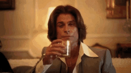 a man in a suit is drinking a glass of whiskey .