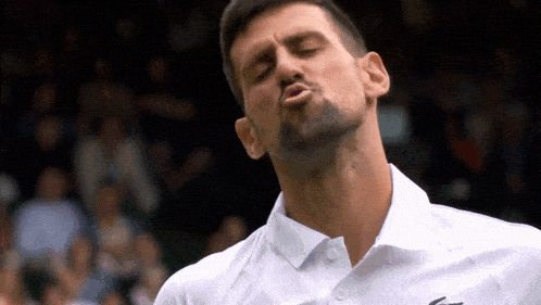 a man with a beard is blowing a kiss while wearing a white shirt .