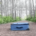 a blue suitcase is sitting on top of a dirt path in the woods .
