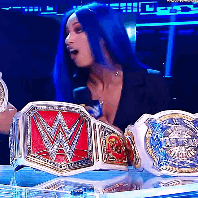 a woman with blue hair is holding a wrestling championship belt with the letter w on it