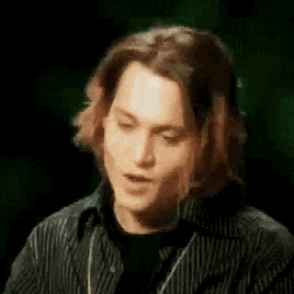 a man with long hair is wearing a black and white striped shirt and a black shirt .