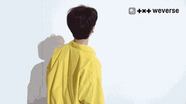 a man in a yellow shirt is standing in front of a white wall with a weverse logo in the corner