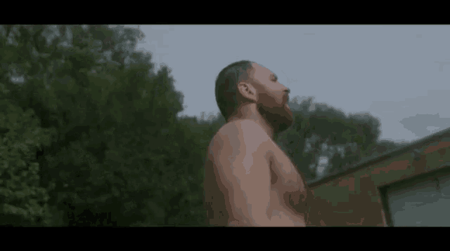a shirtless man with a beard is standing in the rain with his mouth open .