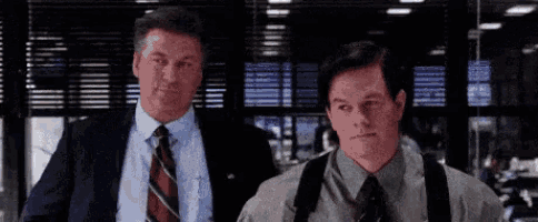 two men in suits and ties are standing next to each other in front of a window .