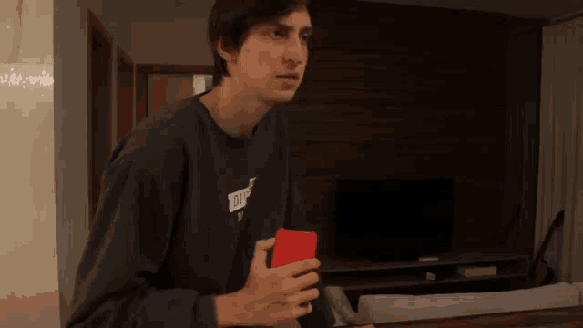 a man wearing a sweatshirt that says ' kith ' on it is holding a red cell phone