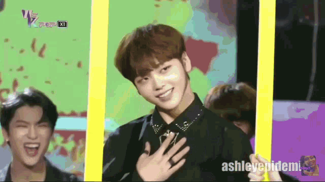 a man in a black shirt is smiling in front of a yellow frame with ashleyepidemi written on the bottom