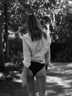 a black and white photo of a woman wearing a striped shirt and black bikini bottoms