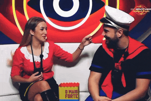 a man and a woman are sitting on a couch in front of a big brother advertisement