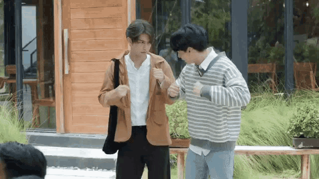 two men are standing next to each other in front of a wooden building .
