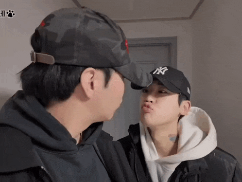 a man wearing a ny hat kisses another man