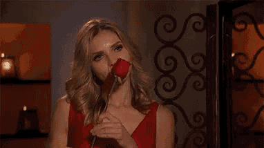 a woman in a red dress is holding a rose in front of her face .