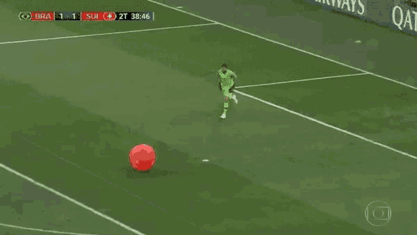 a soccer player is kicking a red ball on a field .