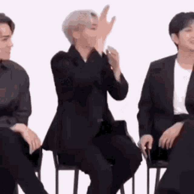 a man in a suit is sitting in a chair while another man applauds him .