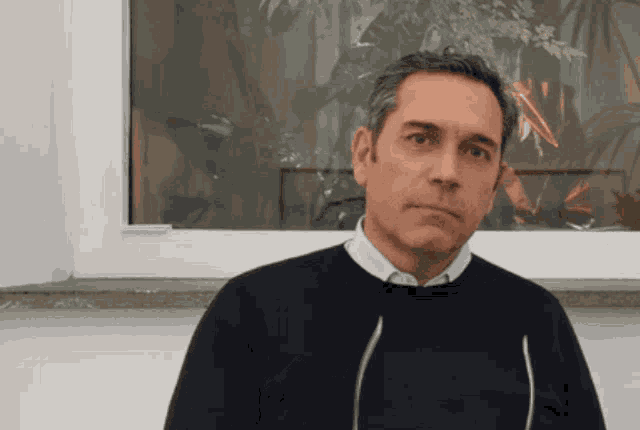 a man in a blue sweater stands in front of a white window
