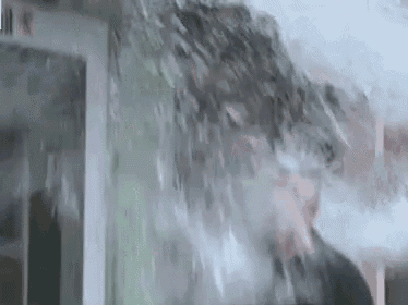 a man is standing in a room with water coming out of the ceiling and a window .