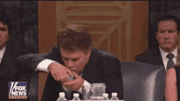 a man in a suit and tie is covering his face while sitting at a fox news conference