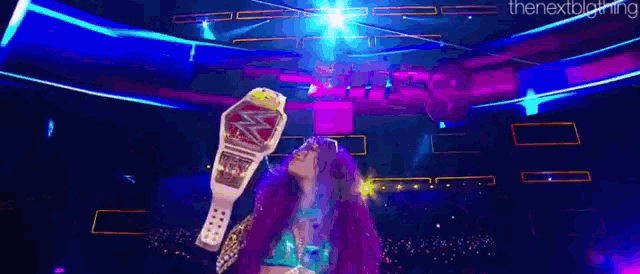 a woman is holding a wrestling championship belt on a stage in a dark room .